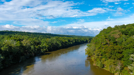 Fototapeta na wymiar a stunning aerial panoramic shot of the Chattahoochee river surrounded by lush green and autumn colored trees with blue sky and clouds at Cochran Shoals Trail in Marietta USA