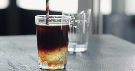 Slow motion add straw to espresso tonic ice ball in tumbler glass on black wood table closeup - Powered by Adobe