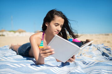 Teenage girl reading at beach. Girl in swimsuit lying on blanket with book. Family, vacation,...
