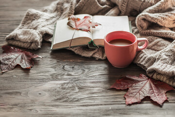 Autumn morning coffee. A cup of coffee on a wooden table and a warm sweater on a background of autumn leaves. Still life concept. Copy space.