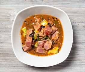 peruvian Tuna ceviche in Tamarind sauce with avocado pieces and seaweed in bowl on gray wooden board