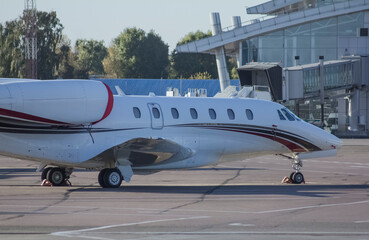 A twin-engine jet business plane with landing lights on is driving along the airport taxiway...