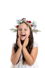 portrait of laughing, charming girl with mouth open in Christmas wreath and in white festive dress holding hands to face with amazement, isolated on white background. 