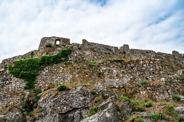 Fototapeta na wymiar Exterior view of the ancient stone walls of the Rozafa Castle in Shkoder (Albania). The dilapidated facade of a medieval fortress, overgrown with plants