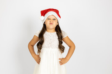 portrait of frowning, dissatisfied girl in Santa Claus hat with hands on waist, isolated on white background, concept of dissatisfaction with New Year gift. 