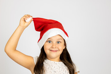 close-up portrait of mischievous, playful girl in red Santa hat holding pompom with hand, isolated on white background with copy space. 