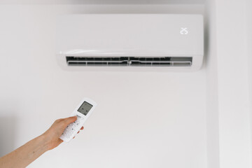 Fototapeta premium Woman holding remote controller against air conditioner