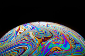 Fototapeta na wymiar Colorful close-up of soap bubble on black background, iridescence phenomenon, looks like rising planet