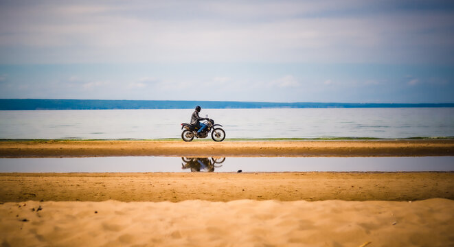 A man on a motorcycle in a helmet rides along the coast. The biker travels. Man, motorcycle and nature.