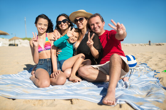 Portrait of smiling family at beach. Happy relatives looking at camera, showing victory sign. Family, vacation, outdoor activity concept