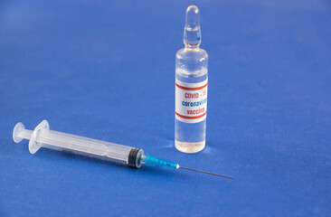 Close-up shot of coronavirus vaccine ampoule and syringe for injection on a blue background....