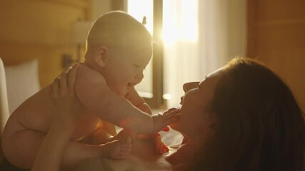 asian woman mother holding baby infant in arm playing and talking with kid on sofa couch in living room at home in evening. happy baby learning communication by smile, laugh, and Stick out tongue. - Powered by Adobe