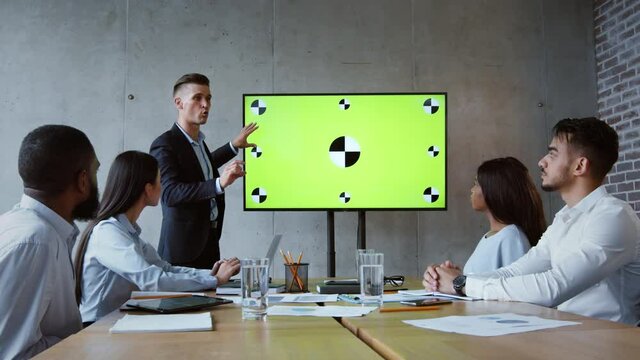 Motivated man boss making presentation to his colleagues, explaining information on green chroma key digital screen