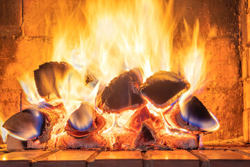 A stack of flaming firewood in a red mud brick fireplace in a country cottage