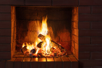 Burning logs and embers in a red brick fireplace in a country cottage