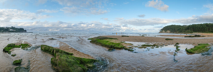 Panoramic view of La Griega beach at low tide, some seagulls on the sand, with a cloudy sky in Lastres, Asturias, Spain