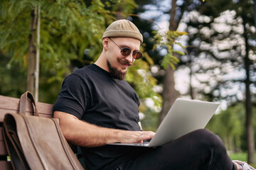 Stylish bearded student chatting working e-learning laptop ps at green park Millennial Hipster 