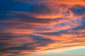Naklejka na ściany i meble Clouds are lit up orange and pink by the light of the low sun. Suitable as background or wallpaper.