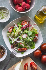 Plato de ensalada de lechuga, tomate, cebolla, rábanos y semillas, rodeado de cuencos e ingredientes