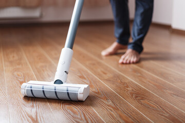 Human legs and a white turbo brush of a cordless vacuum cleaner cleans the parquet in the house.