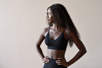 Young fit healthy sporty slim attractive African black woman model fitness coach wearing sportswear standing isolated on grey brown background. Training sport workout gym advertising concept.