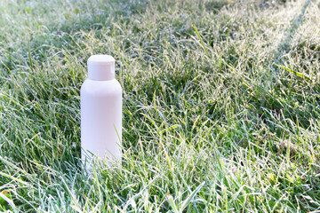 there is a white bottle in the grass with frost and dew drops. aroma of morning freshness