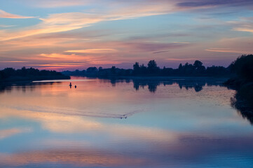 Łódka wędkarze na rzece w pięknym oświetleniu zachodzącego słońca odbicia kolorowych chmur...