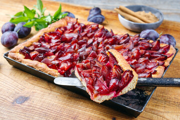 Traditioneller deutscher Zwetschgenkuchen mit geschnittenen Pflaumen serviert als Draufsicht auf einem rustikalen Backblech auf einem Holz Board