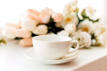 A cup of morning coffee on a background of white tulips