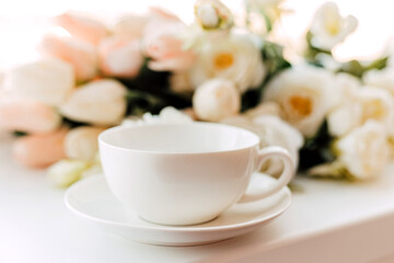 A cup of morning coffee on a background of white tulips