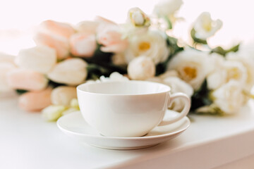A cup of morning coffee on a background of white tulips