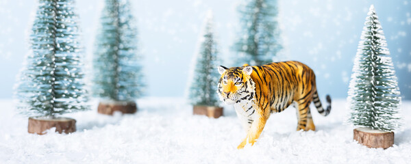 Tiger symbol of the Chinese new year 2022. Figurine of tiger, fir tree and snow on blue background. Christmas greeting card. Banner, copy space.