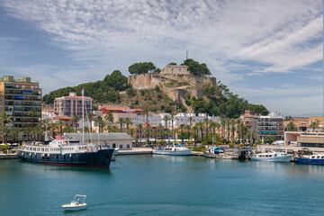 Denia Castle in sunshine with beautiful clouds. In front of it are the houses of the Promeandes. In...