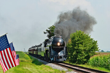 A Antique Restored Steam Engine Approaching Head on Passing a Row of American Flags on a Beautiful Sunny Day