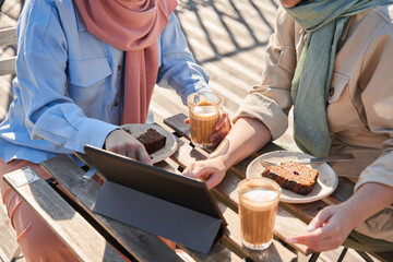 Woman in scarf pointing at the tablet screen while sitting at the cafe with her sister