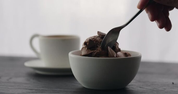 Slow motion eat chocolate ice cream into white bowl with espresso on black wood table