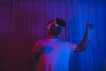 Young man wearing virtual reality glasses in neon lit room.
