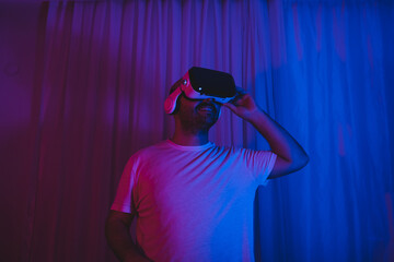 Young man wearing virtual reality glasses in neon lit room.