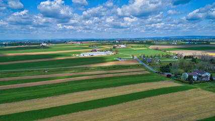 Naklejka premium A Beautiful Aerial View of Farm Countryside with Patches of Colored Fields with White Fully Clouds and Shadows