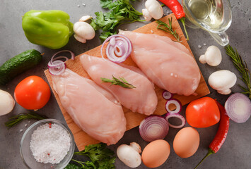 raw chicken fillet with herbs, tomato, onion and oil on a cutting board, salt, parsley, mushrooms, pepper, chili,