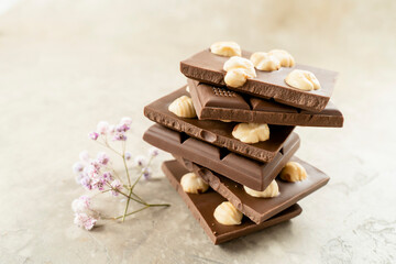 Tower of chocolate pieces with hazelnuts on a white background. Milk chocolate with nuts with a sprig of flowers. Delicious Chocolate for Kids, Holiday, Birthday, Wedding