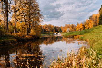 Fototapeta premium View of the Slavyanka River, autumn bright forest and vintage Viscontiev Bridge in the Pavlovsk Palace and Park Complex on a autumn day. Pavlovsk, Saint Petersburg, Russia.