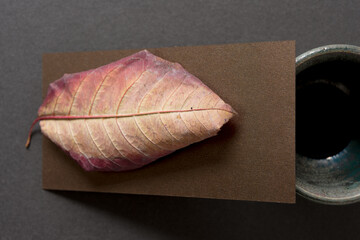 pottery cup, paper, and autumn leaf viewed from above