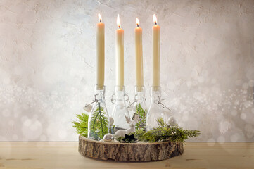 Creative Advent wreath, four lit candles in bottles on a wooden board with fir branches and...