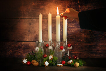First advent, hand lighting one of four candles placed in bottles with fir branches and christmas...