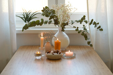 Four different golden burning candles, vase with eucalyptus branches and a bowl with cookies,...