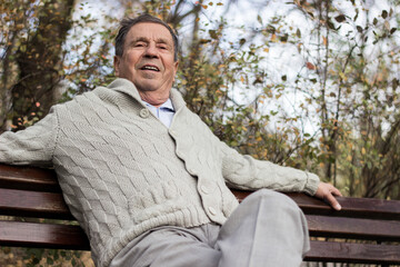 Portrait of a smiling senior man sitting on the bench, in the public park, outdoors.