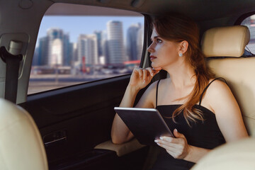 Elegant business woman using tablet computer inside a car on rear seat or vip taxi