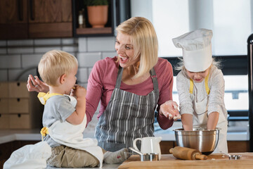 Mother with son and daughter having fun in the kitchen playing with dough, baking