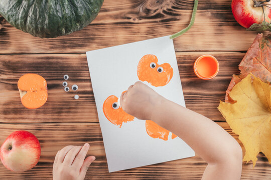 Step-by-step Halloween tutorial pumpkin apple prints. Step 13: Child hand drips drop of glue onto pumpkin print
